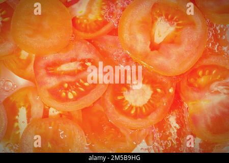 Tomaten-Nahaufnahme in Flüssigkeit mit Blasen. Scheiben roter reifer Tomaten im Wasser. Nahaufnahme frischer Scheiben roter Tomaten auf weißem Hintergrund. Stockfoto