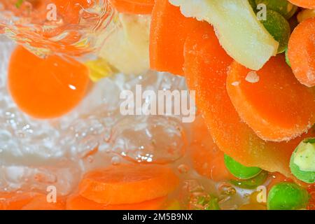 Ich gieße Wasser mit frischem Gemüse, Nahaufnahme. Nahaufnahme des Suppengemüses mit Karotten, Erbsen, Blumenkohl und Mais im Wasserhintergrund Stockfoto