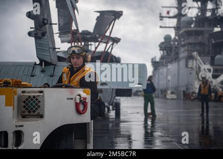 PHILIPPINE SEA (19. Februar 2022) Aviation Boatswain’s Mate (Handling) 3. Class Donald Elliot, Left, aus Kansas City, Mo., zugewiesen an das nach vorn ausgesetzte Amphibienschiff USS America (LHA 6) transportiert einen MH-60s Sea Hawk Hubschrauber vom Helicopter Sea Combat Squadron (HSC) 25 auf dem Cockpit des Schiffes. Amerika, das führende Schiff der America Amphibious Ready Group, ist zusammen mit der 31. Marine Expeditionary Unit im Zuständigkeitsbereich der US-amerikanischen 7.-Flotte tätig, um die Interoperabilität mit Verbündeten und Partnern zu verbessern und als bereitstehende Eingreiftruppe für Frieden und Stabilität in der zu dienen Stockfoto