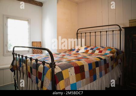 Antikes Messing Doppelbett mit Patchwork-Steppdecke im Hauptzimmer im oberen Stockwerk im alten 1772 französischen Regimestil Haus. Stockfoto