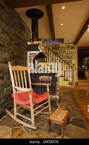 Ein alter Schaukelstuhl aus Holz neben einem antiken, königlichen Holzherd im Speisesaal im Landhausstil. Stockfoto