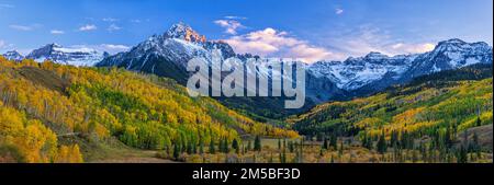 Das letzte Licht der untergehenden Sonne trifft auf die Felsen auf dem Mount Sneffels in den San Juan Mountains. Darunter befindet sich ein überwiegend goldener Hain aus bequetschenden Espen Stockfoto