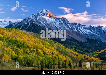 Das letzte Licht der untergehenden Sonne trifft auf die Felsen auf dem Mount Sneffels in den San Juan Mountains. Darunter befindet sich ein überwiegend goldener Hain aus bequetschenden Espen Stockfoto