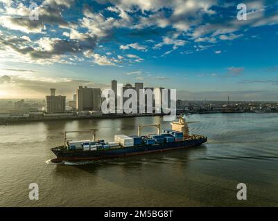 Ein großes Boot voller Fracht fährt an New Orleans vorbei und bietet einen dramatischen Sonnenuntergang am Himmel Stockfoto