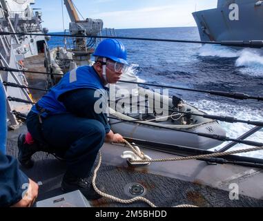 SÜDCHINESISCHES MEER (22. Februar 2022) Seemannsrekruit Koltin Howard aus Paralaine, Texas, stellt während einer Wiederauffüllung auf See mit dem Trockenfrachtschiff der Lewis- und Clark-Klasse USNS Carl Brashear (T-AKE-7) eine Linie an Bord des Arleigh-Burke-Class-Guided-Missile Destroyers USS Ralph Johnson (DDG 114) auf. Ralph Johnson ist der Task Force 71/Destroyer Squadron (DESRON) 15, dem größten nach vorn verlegten DESRON der Marine, und der Hauptstreitkraft der US-7.-Flotte zugewiesen. Stockfoto