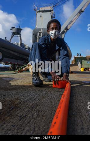 PACIFIC OCEAN (23. Februar 2022) Hospitalman Sabra Nagawa, ein Einheimischer von Masaka Kyazanga, Uganda, rollt einen Feuerwehrschlauch während einer Schulung zur Schadensbegrenzung an Bord des Amphibiendock-Landungsschiffs USS Pearl Harbor der Harpers Ferry-Klasse (LSD 52) im Pazifischen Ozean, 23. Februar 2022. Matrosen und Marines der Essex Amphibious Ready Group (ARG) und der 11. Marine Expeditionary Unit (MEU) führen derzeit Routineeinsätze in der US-amerikanischen 3.-Flotte durch. Stockfoto