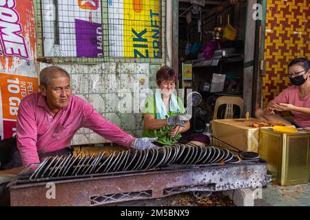 Pulau Ketam, Malaysia - 26. Dezember 2022: Pulau Ketam bedeutet Krabbeninsel, eine kleine Insel vor der Küste von Klang. Ein altes Paar, das lokale Waffeln herstellt, Stockfoto