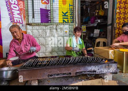 Pulau Ketam, Malaysia - 26. Dezember 2022: Pulau Ketam bedeutet Krabbeninsel, eine kleine Insel vor der Küste von Klang. Ein altes Paar, das lokale Waffeln herstellt, Stockfoto