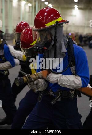 Aviation Boatswains Mate (Handling) Airman Ryan Newbill, aus Elkhart, Indiana, dem Luftwaffenbüro von USS Gerald R. Ford (CVN 78) zugeteilt, bekämpft ein simuliertes Feuer, während der Düsenmann während einer allgemeinen Quartierübung in der Hangarbucht am 24. Februar 2022 ein simuliertes Feuer bekämpft. Ford liegt im Hafen der Newport News Shipyard und begeistert ihre geplante inkrementelle Verfügbarkeit (PIA), eine sechsmonatige Periode der Modernisierung, Wartung und Reparatur. (USA Marinefoto von Mass Communication Specialist Seaman Apprentice Manvir Gill) Stockfoto