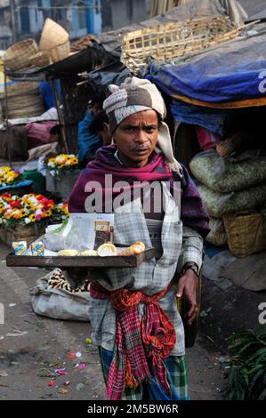 Ein bengalischer Mann, der auf dem Blumenmarkt von Mallick Ghat in Kalkutta, Indien, Sahnepuffs verkauft. Stockfoto