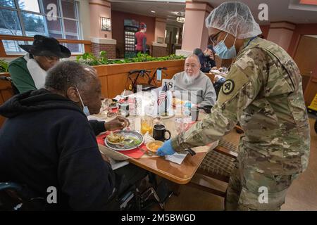 USA Army SPC. Rayas Ali, Charlie Company, 104. Brigade Engineer Battalion, 44. Infanterie Brigade Combat Team, New Jersey Army National Guard, Hands James Dow, ein Bewohner des New Jersey Veterans Memorial Home in Vineland, seine Wüste im Home's Dining Room in Vineland, New Jersey, 24. Februar 2022. Ebenfalls abgebildet sind Alphonso Smith, links, und Leroy Pierce, das zweite von rechts. Ali bedient die Bewohner des Heims in der Abteilung für Lebensmitteldienste. Mehr als 70 Soldaten der New Jersey National Guard und Airmen dienen als zertifizierte Pflegehelfer und in Food Services, Infection Contr Stockfoto