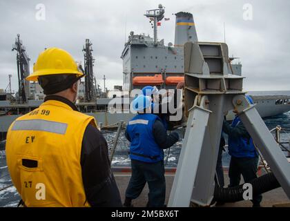 220224-N-EH998-1125 ATLANTISCHER OZEAN (24. Februar 2022) Seeleute an Bord des Routenplanetenzerstörers USS Farragut (DDG 99) befestigen während einer Wiederauffüllung auf See vom USNS John Lenthall (T-AO 189) eine Treibstoffleitung, während sie sich auf dem Weg zum Surface Warfare Advanced Tactical Training (SWATT) befinden. Farragut ist Teil der Destroyer Squadron (DESRON) 26, die die Carrier Strike Group (CSG) 10 unterstützt. SWATT wird vom Naval Surface and Mine Warfighting Development Center (SMWDC) geleitet und soll die Kampffähigkeit, die Letalität und die Interoperabilität der teilnehmenden Einheiten verbessern. Stockfoto