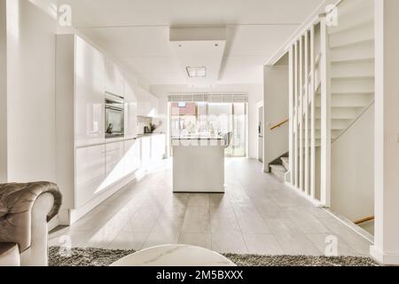 Küche und Essbereich in einem Haus mit weißen Schränken, Marmorboden und einer offenen Treppe, die zum Wohnzimmer führt Stockfoto