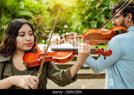 Violinistin und Violinistin spielen im Park im Freien. Zwei junge Violinisten, die in einem Park Geige spielen. Porträt des Menschen und Stockfoto