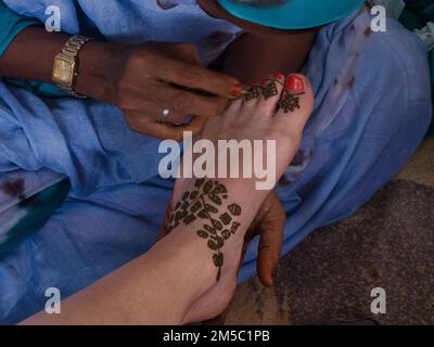 Eine Nahaufnahme einer Frau, die mit Henna auf dem Fuß einer Frau über einem blauen Tuch malt Stockfoto