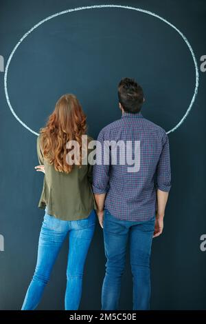 Aus einem anderen Blickwinkel betrachtet. Rückblick auf ein junges Paar, das einen leeren Kreis auf einer Tafel sieht. Stockfoto