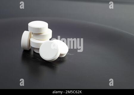 Auf einer keramischen Oberfläche mit schwarzem Hintergrund gestapelte Tabletten oder Tabletten. Gesundheitswesen und Medizin, Soft Focus Nahaufnahme Stockfoto