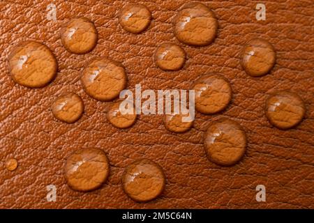 Runde Wassertropfen auf brauner Lederstruktur, weiches Fokusmuster für Nahaufnahmen Stockfoto