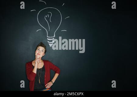 Stellen Sie sich die Möglichkeiten vor. Studioaufnahme einer jungen Frau, die posiert, mit einer Kreidezeichnung einer Glühbirne vor einem dunklen Hintergrund. Stockfoto