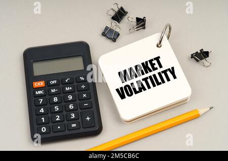 Geschäftskonzept. Auf einer grauen Oberfläche, einem Taschenrechner, einem Bleistift und einem Notizblock mit der Aufschrift "Marktvolatilität" Stockfoto