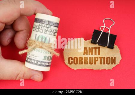 Geschäftskonzept. Der Mann hat Geld in der Hand, auf einer roten Oberfläche ist ein Pappschild mit der Aufschrift "Anti Corruption" Stockfoto