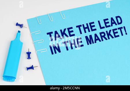 Wirtschaftskonzept. Auf einer weißen Oberfläche, mit einem Marker, Knöpfen und einem blauen Blatt Papier mit der Aufschrift – übernehmen Sie die Führung auf dem Markt Stockfoto