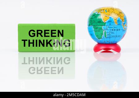 Ökologisches Konzept. Auf einer reflektierenden Oberfläche befinden sich ein Globus und ein grünes Zeichen mit der Inschrift „Green Thinking“ Stockfoto