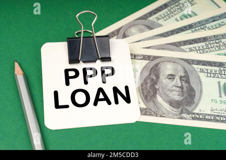 Geschäftskonzept. Auf einer grünen Oberfläche, einem Stift, Dollars und in einem Heftpapier mit der Aufschrift "PPP-Kredit" Stockfoto