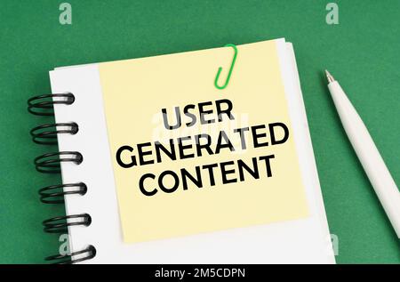 Geschäftskonzept. Auf einer grünen Oberfläche: Ein Stift, ein Notizblock mit Aufklebern und die Aufschrift „User Generated Content“ Stockfoto
