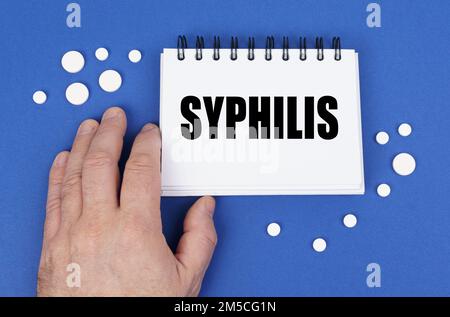 Medizinisches Konzept. Auf der blauen Oberfläche der Tablette eine Hand und ein Notizblock mit der Aufschrift - SYPHILIS Stockfoto