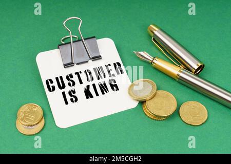 Geschäfts- und Finanzkonzept. Auf einer grünen Oberfläche befinden sich ein Stift, Münzen und ein Notizblock mit der Aufschrift „Kunde ist König“