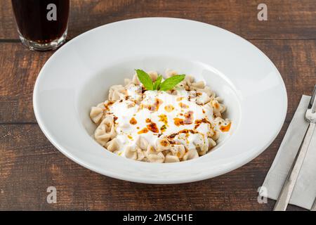 Kayseri ravioli oder Kayseri Mantisi auf einem weißen Teller auf einem Holztisch Stockfoto