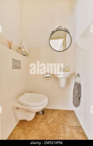 Ein Badezimmer mit Toilette, Waschbecken und Spiegel an der Wand daneben ist ein Handtuch, das auf dem Regal hängt Stockfoto