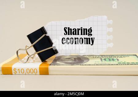 Geschäftskonzept. Auf einer grauen Oberfläche befindet sich eine Packung Dollar, auf der ein Clip mit zerrissenem Papier und die Inschrift "Sharing Economy" steht Stockfoto