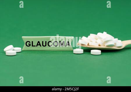 Medizinisches Konzept. Auf einer grünen Oberfläche, einem Holzlöffel mit Pillen und einem Schild mit der Inschrift - GLAUKOM Stockfoto