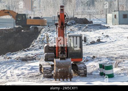 Orangefarbene und gelbe Raupenbagger auf einer Baustelle im Winter Stockfoto