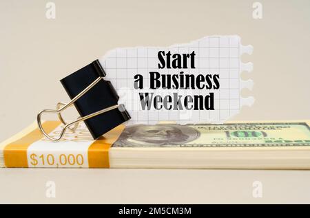 Geschäftskonzept. Auf einer grauen Oberfläche befindet sich eine Packung Dollar, auf der ein Clip mit zerrissenem Papier und die Aufschrift „Start a Business Weekend“ (ein Geschäftswochenende beginnen) angebracht sind Stockfoto