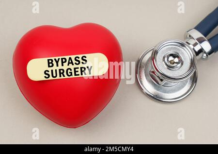 Medizinisches Konzept. In der Nähe des Stethoskops befindet sich ein Herz, auf das ein Aufkleber mit der Aufschrift „Bypass Surgery“ (Bypass-Chirurgie) aufgeklebt wird Stockfoto