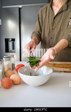 Nicht wiedererkennbarer junger asiatischer Mann, der gehackten chinesischen Schnittlauch in eine Schüssel steckt. Stockfoto