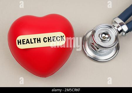 Medizinisches Konzept. In der Nähe des Stethoskops liegt ein Herz, auf dem ein Aufkleber mit der Inschrift - HEALTH CHECK geklebt wird Stockfoto