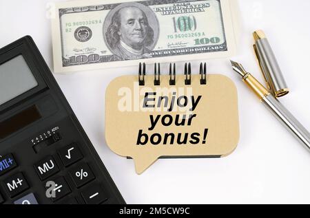 Geschäftskonzept. Auf einer weißen Oberfläche, einem Taschenrechner, einem Dollar, einem Stift und einem Schild mit der Inschrift – genießen Sie Ihren Bonus Stockfoto