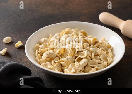 Gesunde hausgemachte trockene Orecchiette Pasta in der Schüssel auf brauner Tischplatte. Schließen. Stockfoto