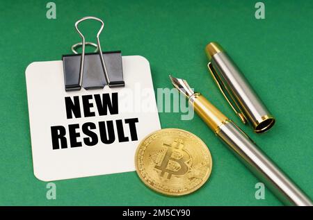 Kryptowährung und Geschäftskonzept. Auf einer grünen Oberfläche eine Bitcoin, ein Stift und ein Blatt Papier mit der Aufschrift „Neues Ergebnis“ Stockfoto