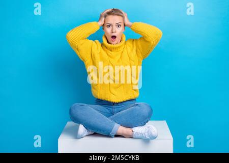 Das Foto einer verblüfften, peinlichen Dame, die auf der Plattform saß, beeindruckte schlechte Nachrichten Negative Informationen isoliert auf blauem Hintergrund Stockfoto