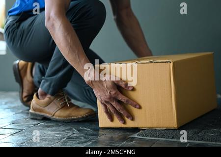 Zugeschnittenes Bild eines männlichen Kuriers, der Pappkartons in der Nähe des Eingangs platziert. Lieferservice und Versandkonzept Stockfoto