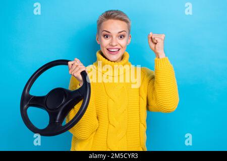 Foto einer überfreulichen Frau trägt einen stilvollen gelben Pullover hebt die Faust Freude kauft ein neues eigenes Auto isoliert auf blauem Hintergrund Stockfoto