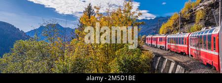 CADERA, SCHWEIZ - OKTOBER 28,2022: BERNINA Express of Rhaetian Railway Line, die an einem farbenfrohen Herbsttag bis zum Berner Berg fährt Stockfoto