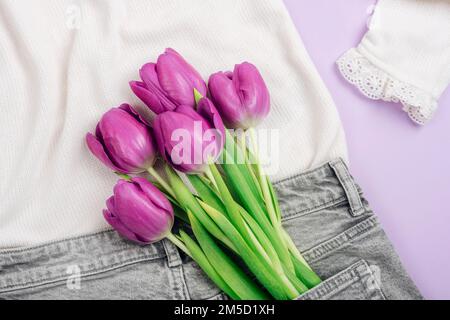Ein Strauß lila Tulpen in einer Tasche grauer Jeans. Frühjahrsferien-Konzept. Draufsicht, flach liegend Stockfoto