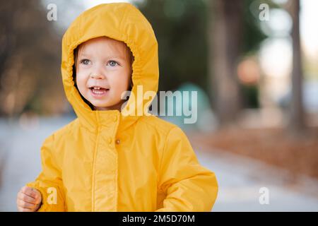 Süßes, lustiges 2-3-jähriges Mädchen trägt im Herbstpark im Freien eine gelbe Regenjacke mit Kapuze. Herbstsaison. Kindheit. Stockfoto