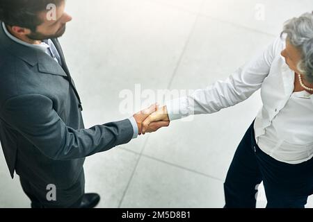 Lass uns Geschäfte machen. Aufnahmen aus einem hohen Blickwinkel von Geschäftsleuten, die sich in einem modernen Büro die Hand schütteln. Stockfoto